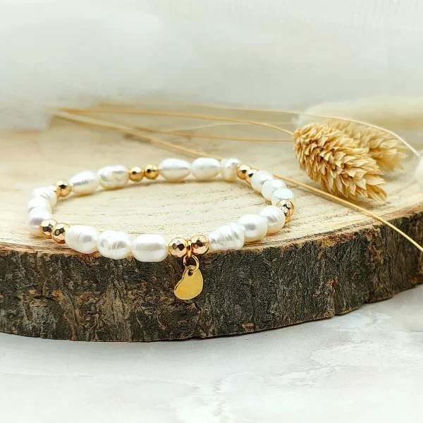 bransoletka z pereł ze złotą przywieszką w kształcie serca leży na drewnianej podstawce.